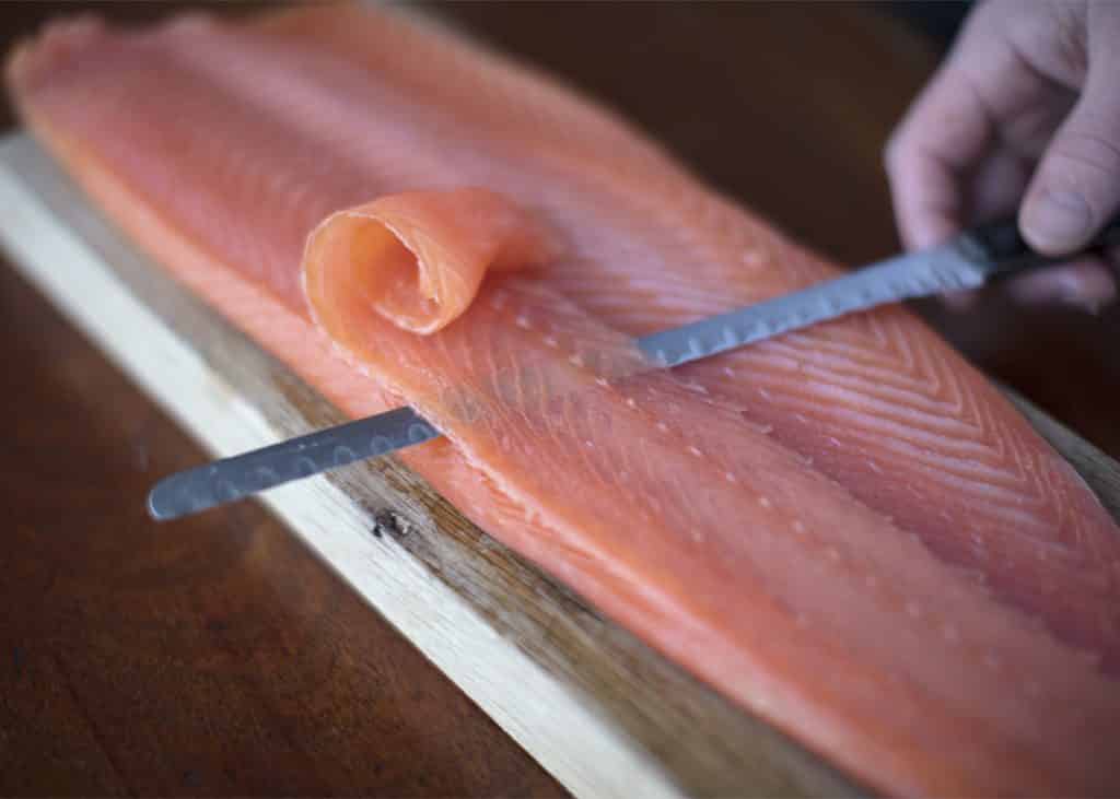 Side of smoked salmon being carved with thin knife