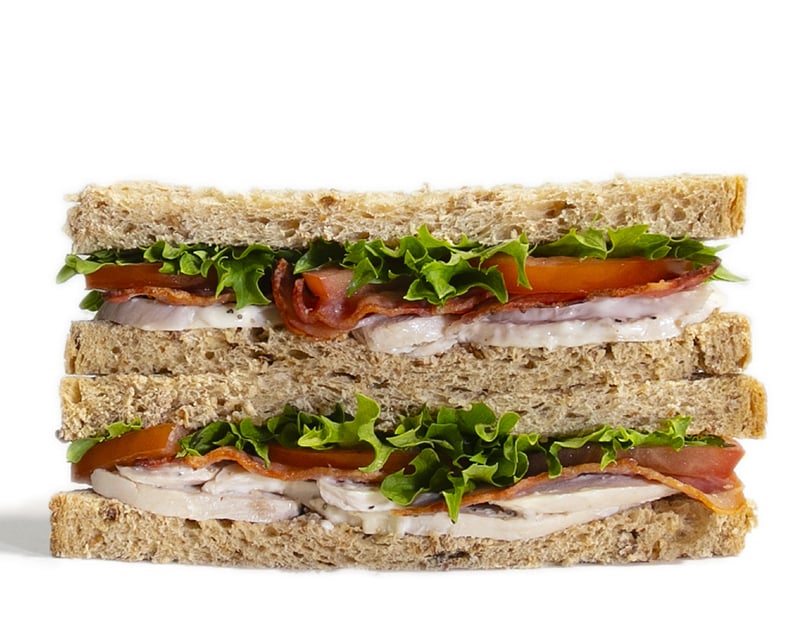 Chicken club sandwich bursting with filling between brown bread on white background